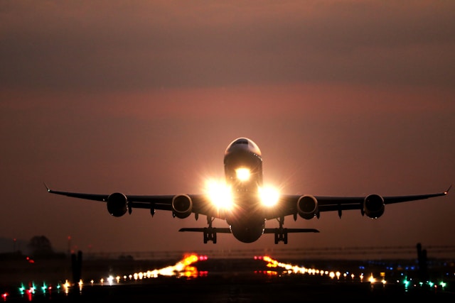 A large commercial aircraft taking off from a runway at sunrise or sunset, with its bright landing lights illuminating the path, symbolizing rapid global air freight, expedited shipping, and worldwide connectivity.